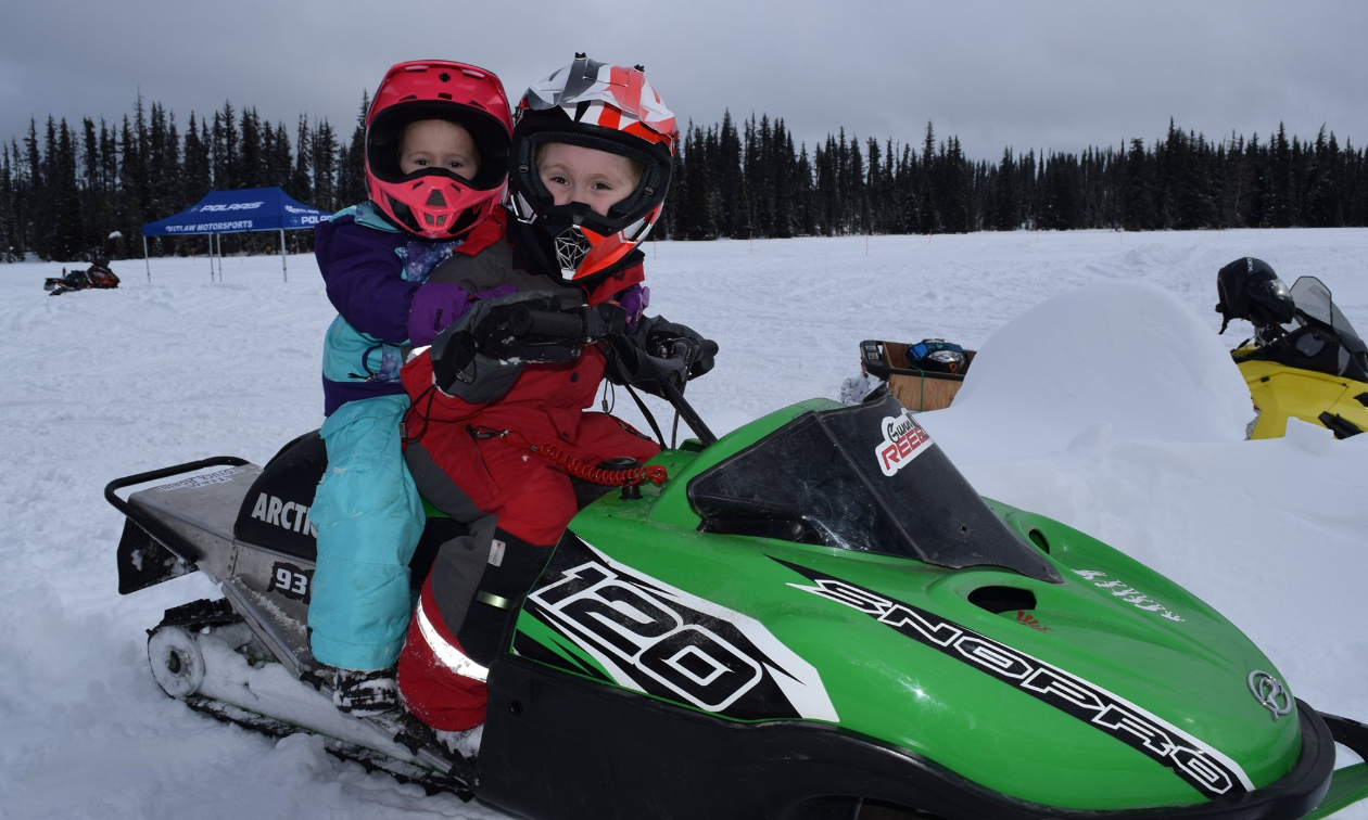 Two children ride a green snowmobile. 