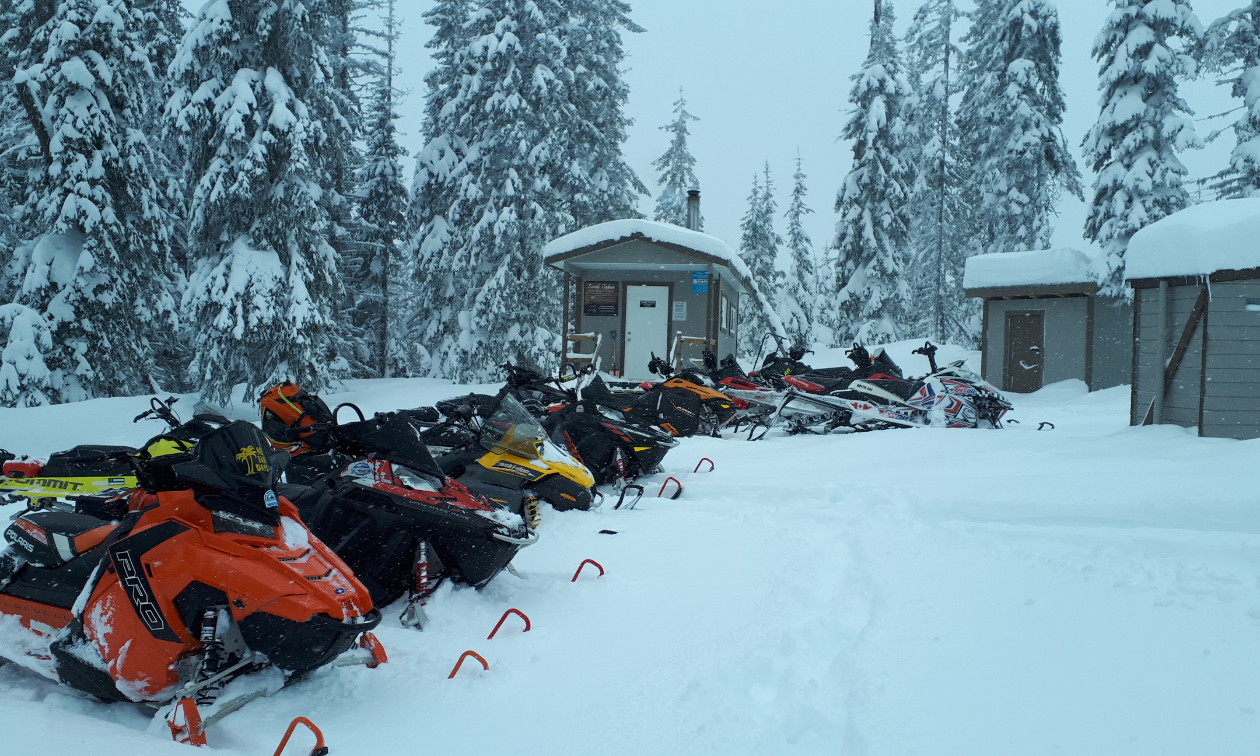 A row of snowmobiles lines the snow in front of several small warm-up shelters in Kamloops. 