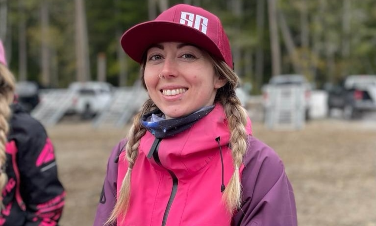 Kirsten Patton smiles. She has shoulder-length blonde braided hair. She wears a pink hat and a pink coat. 