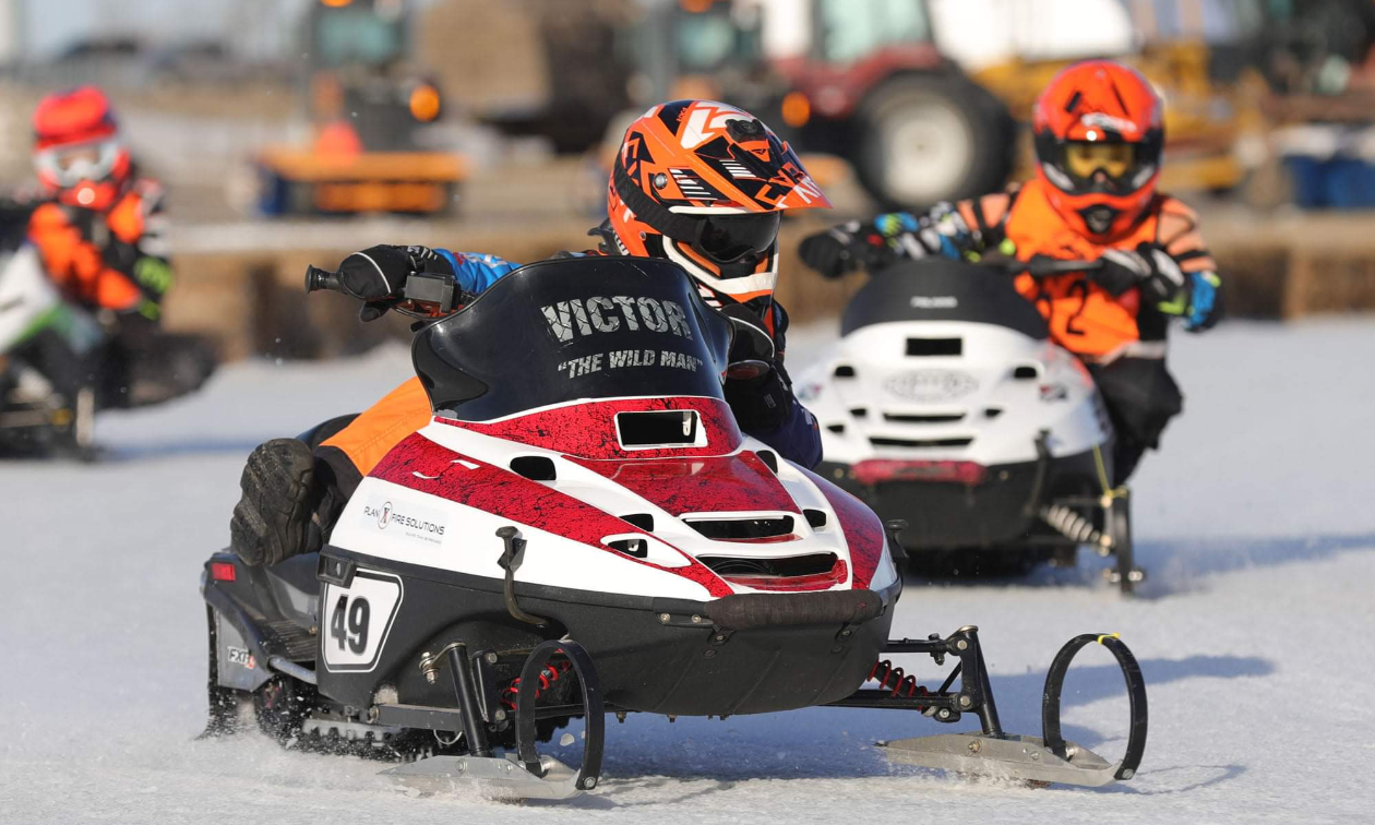 A small child races a snowmobile on an ice oval track. 