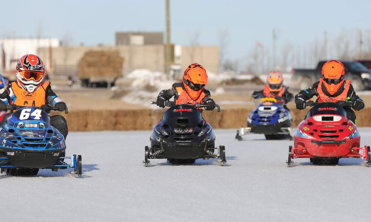 Four young snowmobilers race around an ice oval track in Beausejour, Manitoba. 