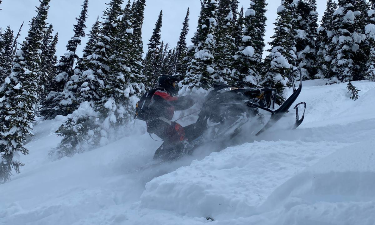 A snowmobiler plows through white powder snow while leaning back.