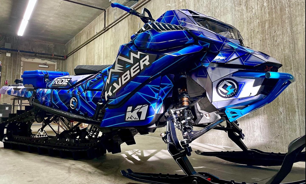 A dark blue snowmobile is parked in a gray carport. 