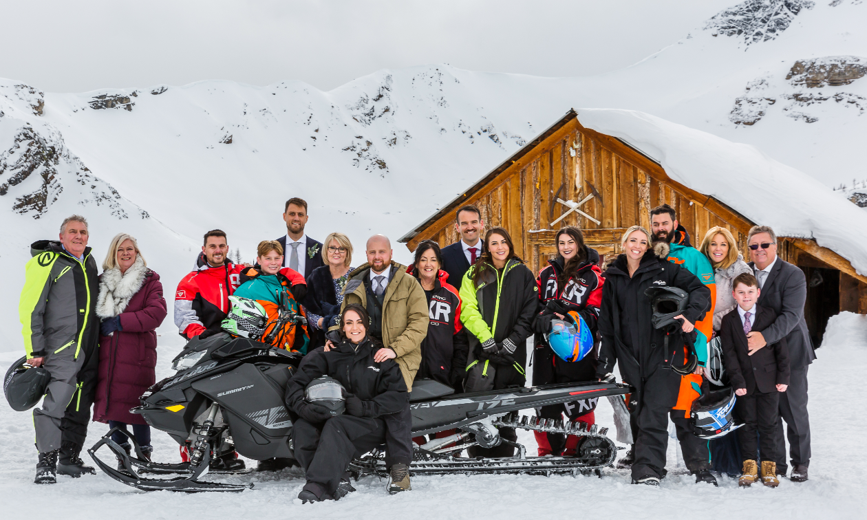 At Toby Creek Lodge, a group of wedding guests pose behind a black snowmobile. 