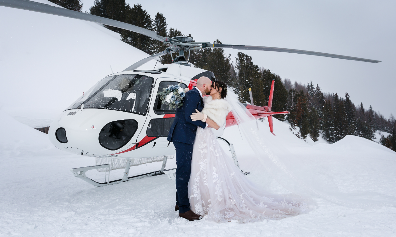 Sarah and Damian Liebeknecht kiss in front of a helicopter in B.C.’s Purcell Mountains. 