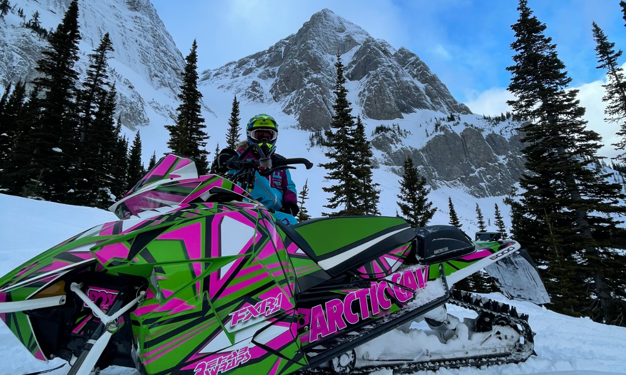 Madison Schwengler sits on her black and pink 2017 Arctic Cat M 6000 Mountain Cat 153 in the shadow of a mountain. 