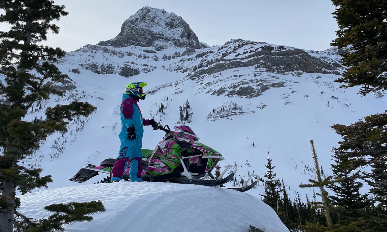 Madison Schwengler stands next to her 2017 Arctic Cat M 6000 Mountain Cat 153 on the crest of a mountain. 