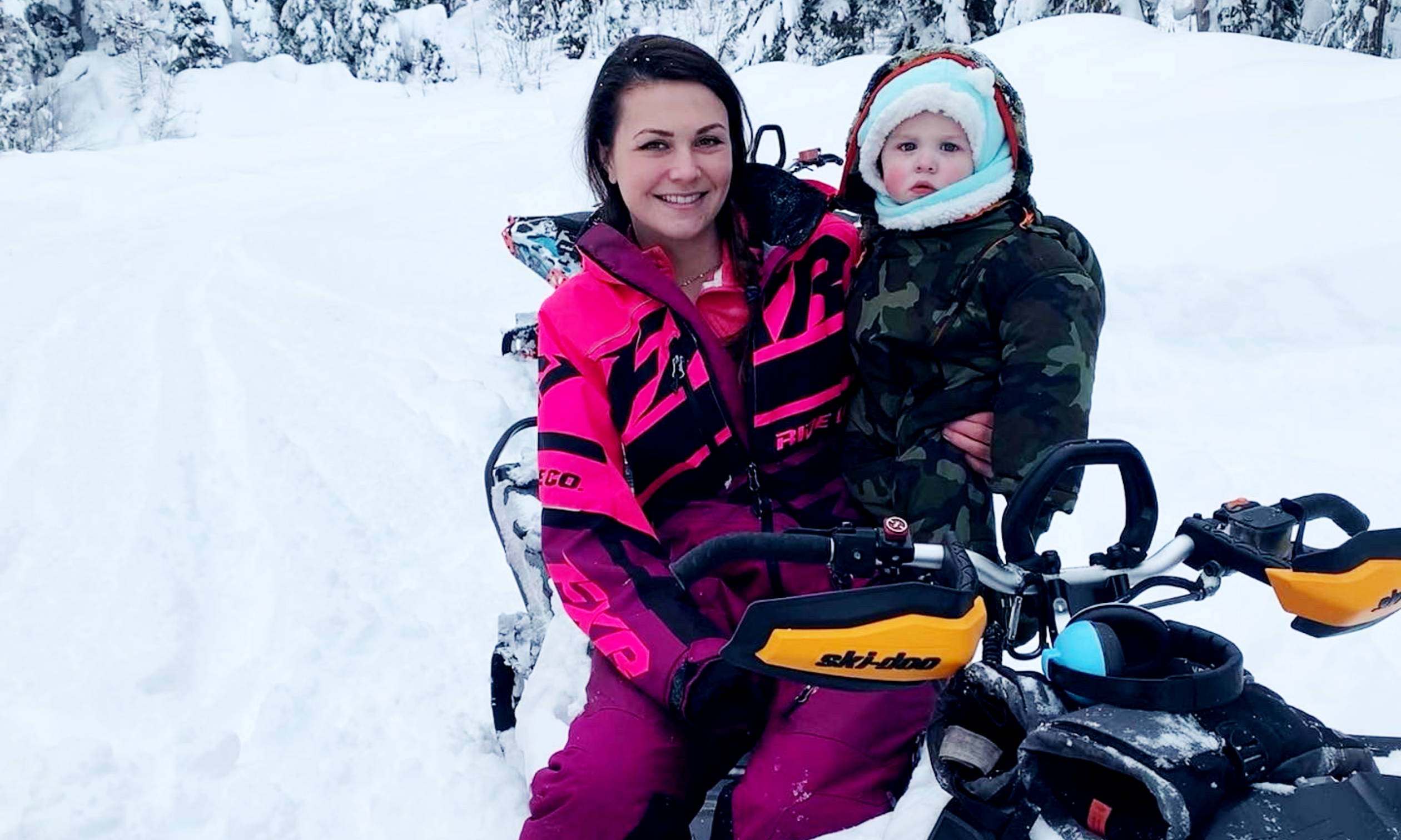 Shelby Ingram wears a pink snowsuit while sitting on a snowmobile with her one-year-old son, Mason Chomica.