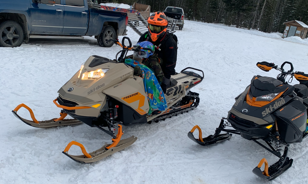 Bobby Chomica sits on a tan snowmobile with his son Mason Chomica. 