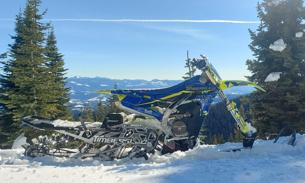 A blue and green Timbersled snow bike on top of a mountain. 