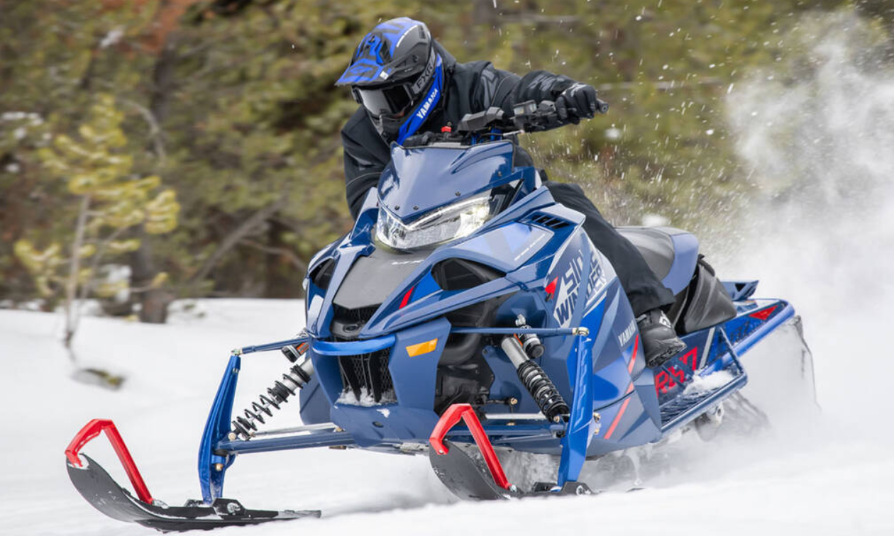 A snowmobiler leans right into a turn on his blue Yamaha sled. 