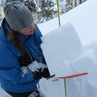 A woman holding a broken layer of snow on a shovel. 