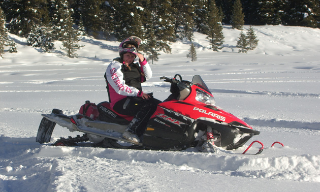 Photo of a girl siting on a red snowmobile with snow and trees in the background