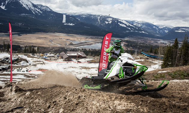 A man on a white and green Arctic Cat riding up a hillclimb. 