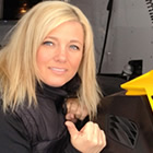 Photo of a blonde haired woman crouching beside a yellow and black snowmobile in an enclosed snowmobile trailer.