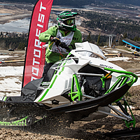 A man on a white and green Arctic Cat riding up a hillclimb. 