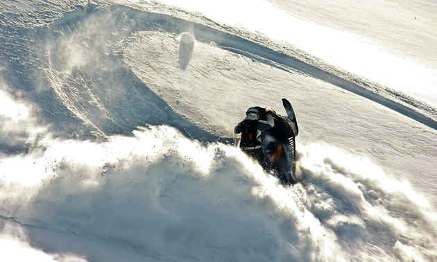 A guy on a black sled spinning on a sidehill. 
