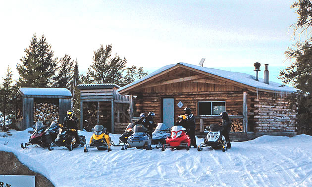 A group of snowmobilers rest in from of Red Rock Lake Shelter.