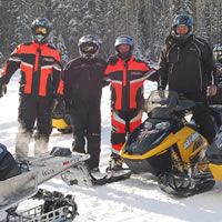 A group of snowmobilers standing on the trails. 
