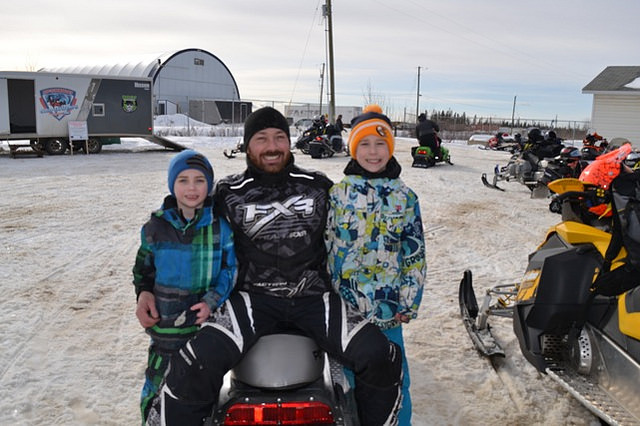 A man with two children sitting on a snowmobile.