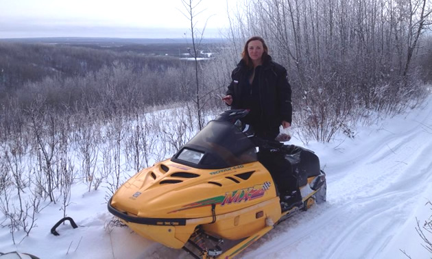 A dark haired woman on a yellow snowmobile. 