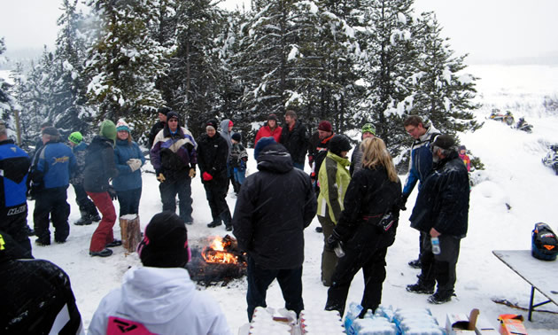 A group of snowmobilers gathered around a fire. 