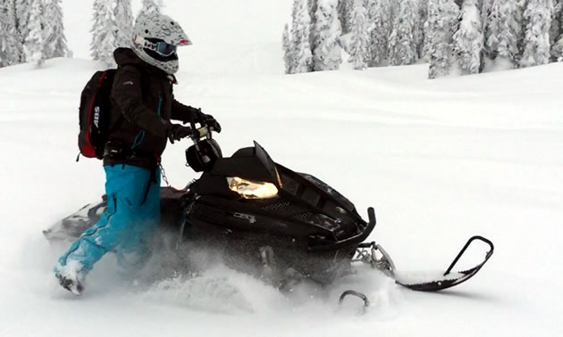 A women riding wrong foot forward on a black Polaris sled. 