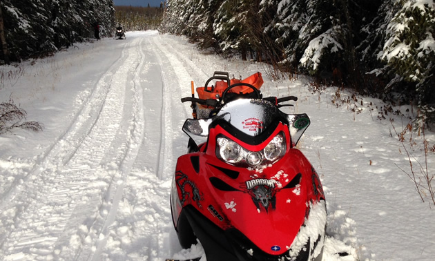 A red sled sitting at the side of a snowmobile trail. 