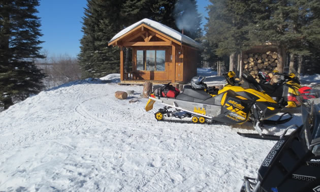 Two snowmobiles parked in front of a little cabin. 