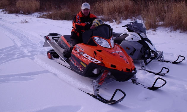 A man sitting on an orange M1000 snowmobile. 