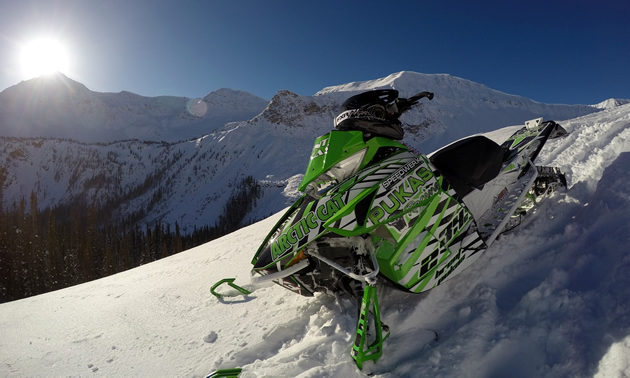 A green Arctic Cat sitting on top of a mountain with the sun in the background. 