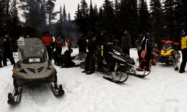 A group of snowmobilers gathered around a fire. 