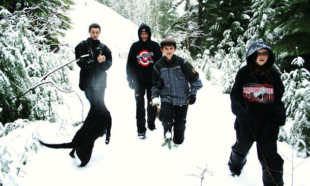 A mother and her three kids walking with a dog through the snow. 