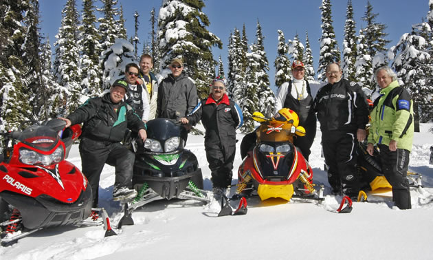 A group of snowmobilers parked on a mountain. 