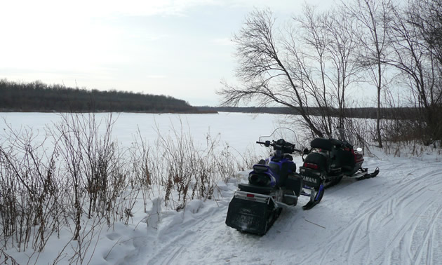 Snowmobiles parked beside a snow covered lake. 