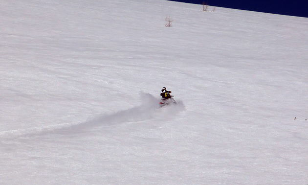 A man climbing a steep hill on a Timbersled snow bike. 