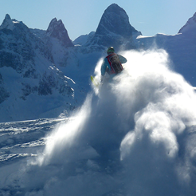 Snow billowing behind a snowmobiler who was jumping and the Bugaboo spires in the distance. 