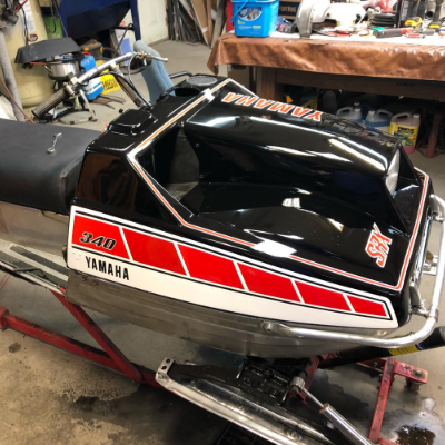 This black vintage snowmobile has red squares along the side with a white stripe underneath 