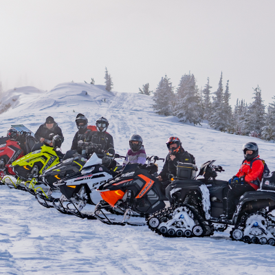 Snowmobilers pose on snowy trail.