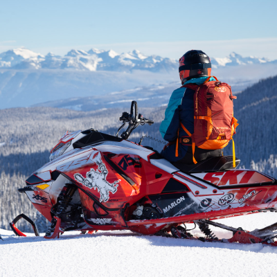 David Norona sits on his snowmobile, looking into the mountains in the distance.