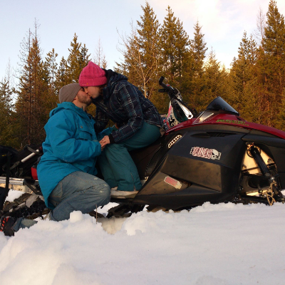 Drew and Liane Leger kiss each other while sitting on a snowmobile.