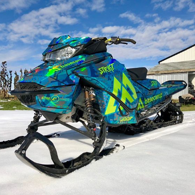 A bluish-green sled wrap on a snowmobile on a beautiful bluebird day.