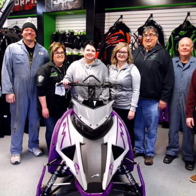 A group of workers pose behind a snowmobile inside Universe Satellite Sales.