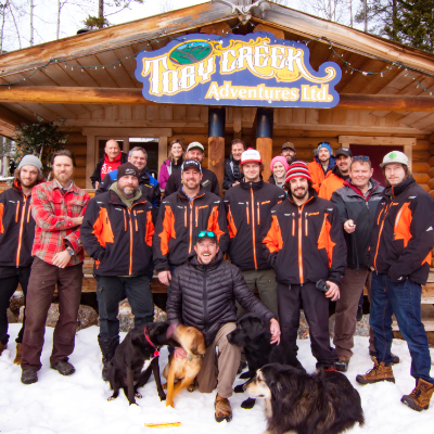 The staff of Toby Creek Adventures pose in front of a cabin with the name of the business on it.