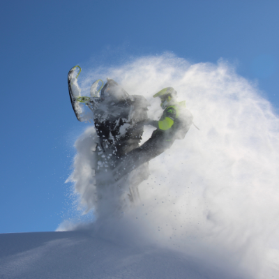A snowmobiler does a wheelie in the midst of a cloud of snow. 