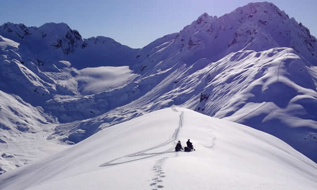 Two snowmobilers sitting on top of a ridge in Valdez, Alaska. 