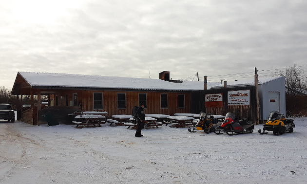 The Braeburn Lodge is brown with a few snowmobiles parked up front.