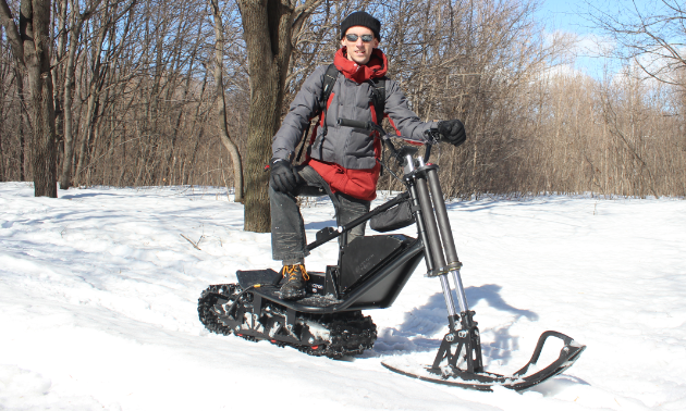 A man poses on an electric snow scooter. 