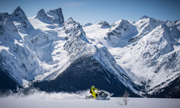 A snowmobile shreds through snow in front of towering mountains. 