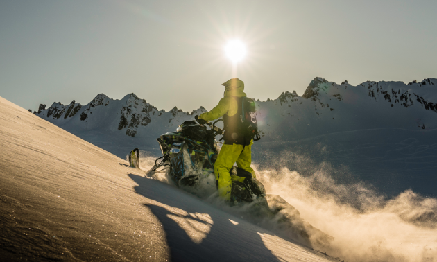 A snowmobile glides up a mountain as the sun casts shadows in the distance. 